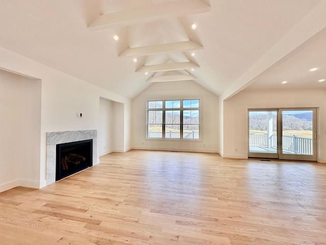 unfurnished living room with a healthy amount of sunlight, a high end fireplace, beam ceiling, and light hardwood / wood-style floors