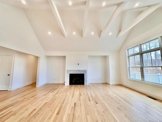 unfurnished living room featuring beamed ceiling, high vaulted ceiling, a premium fireplace, and light hardwood / wood-style floors