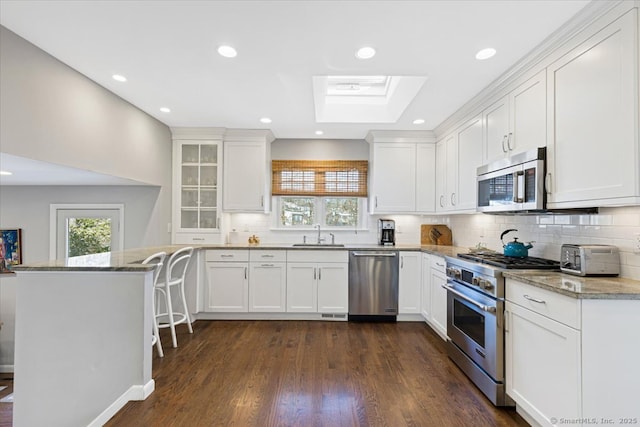 kitchen with white cabinetry, light stone counters, kitchen peninsula, and appliances with stainless steel finishes