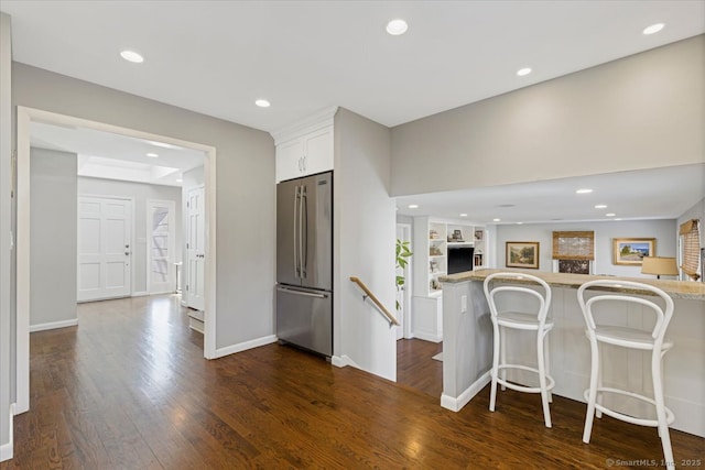 kitchen with dark wood-type flooring, a breakfast bar area, stainless steel fridge, kitchen peninsula, and white cabinets