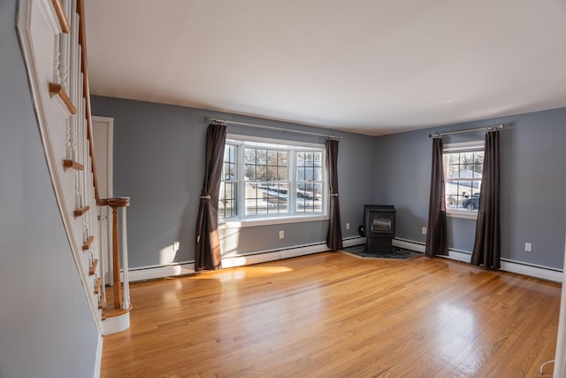 empty room with a baseboard heating unit, a wood stove, and light hardwood / wood-style flooring