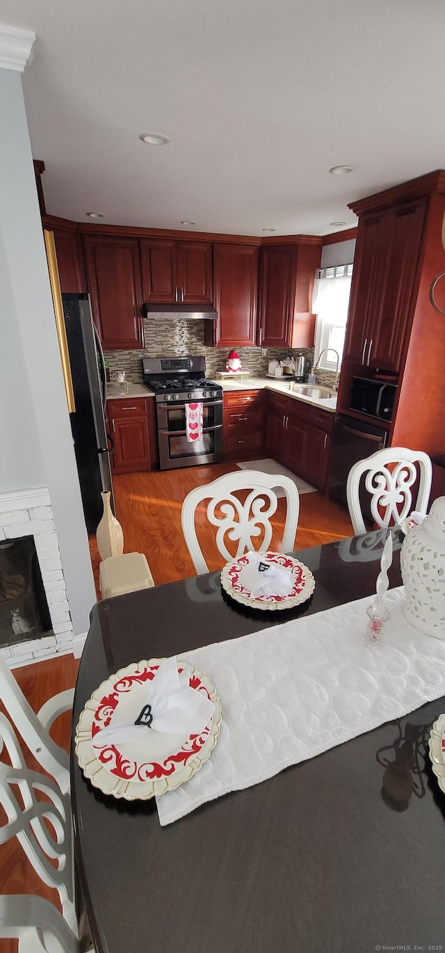 kitchen with a fireplace, wood-type flooring, sink, backsplash, and stainless steel appliances