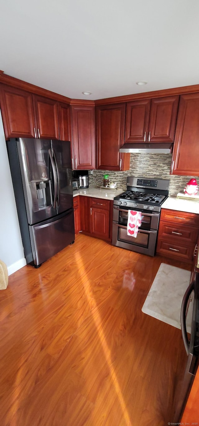 kitchen with appliances with stainless steel finishes, decorative backsplash, and light wood-type flooring