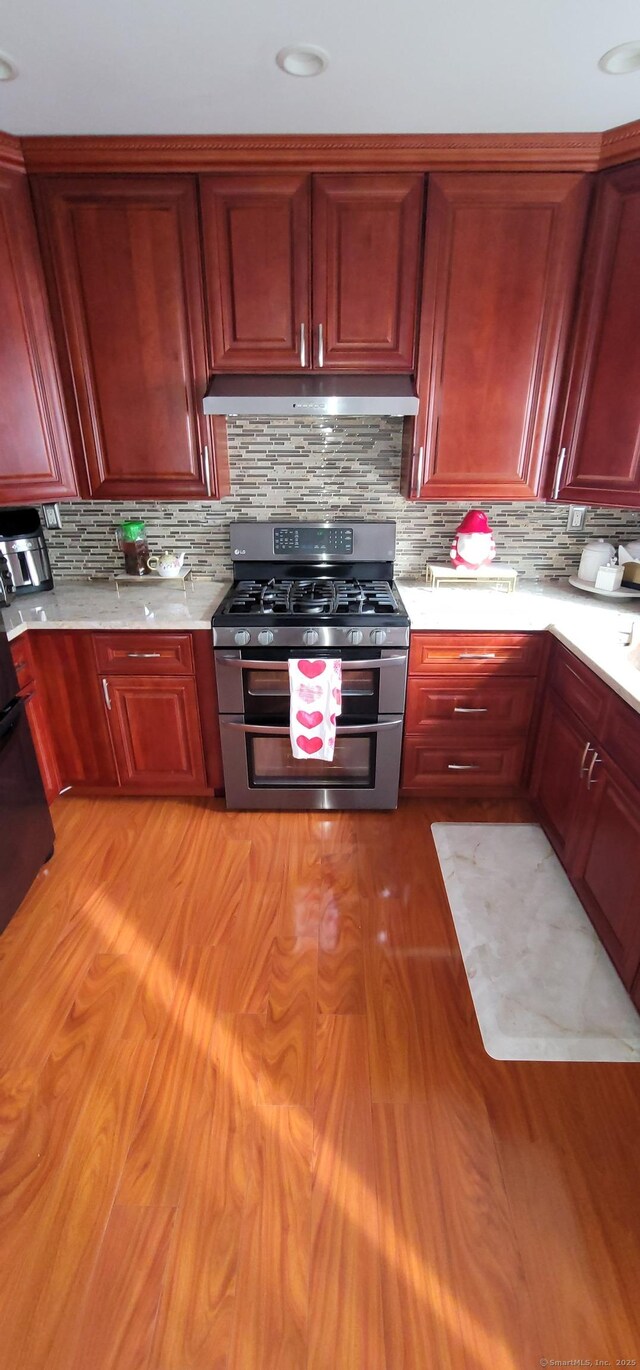 kitchen with tasteful backsplash, light wood-type flooring, range with two ovens, and exhaust hood