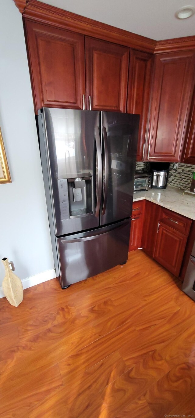 kitchen featuring decorative backsplash, stainless steel fridge, light stone counters, and light hardwood / wood-style flooring