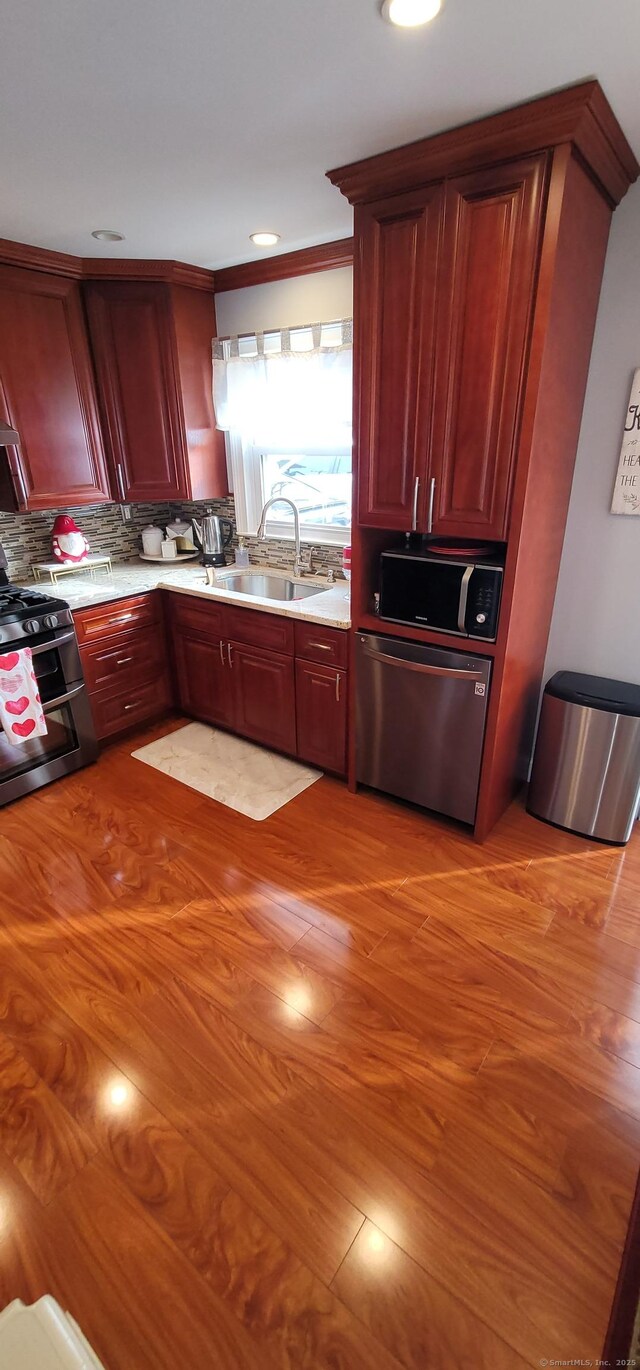 kitchen with appliances with stainless steel finishes, sink, backsplash, and light hardwood / wood-style flooring