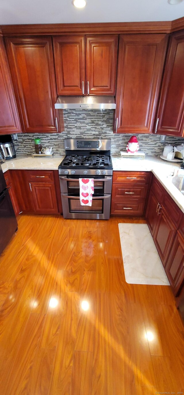 kitchen featuring double oven range, ventilation hood, light hardwood / wood-style flooring, and backsplash