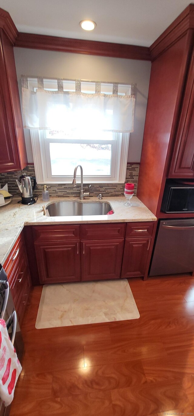 kitchen with dishwasher, sink, backsplash, light stone counters, and light hardwood / wood-style floors