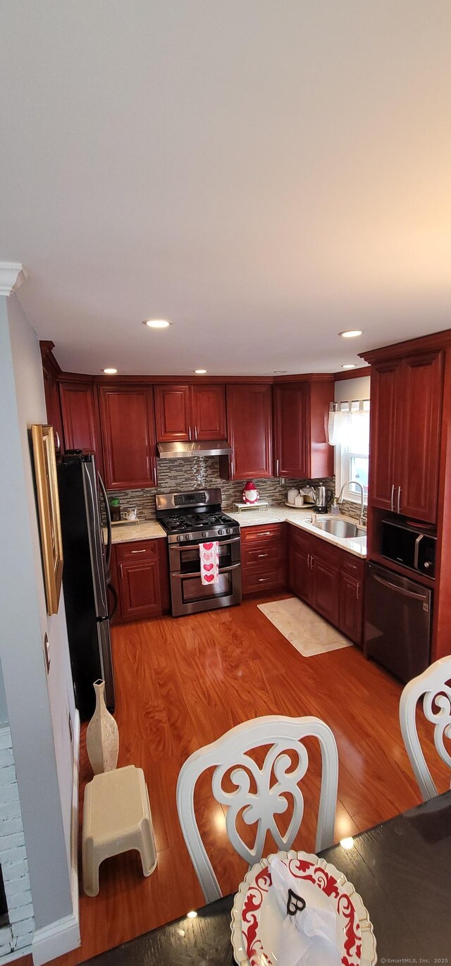 kitchen featuring appliances with stainless steel finishes, sink, light hardwood / wood-style flooring, and backsplash