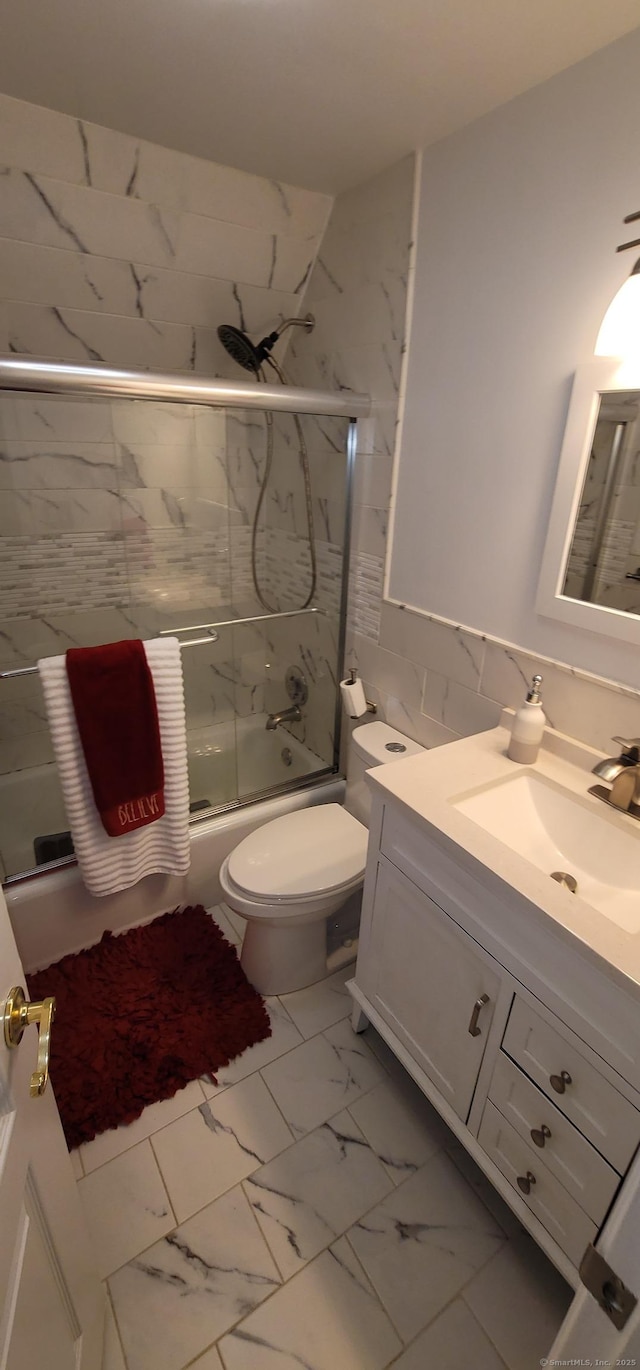 full bathroom featuring vanity, combined bath / shower with glass door, tile walls, and toilet