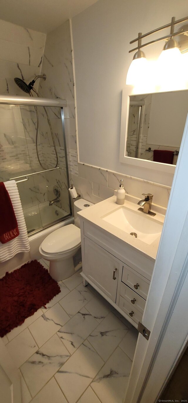 full bathroom with bath / shower combo with glass door, tile walls, vanity, and toilet