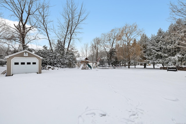 yard layered in snow with an outbuilding, a garage, and a playground