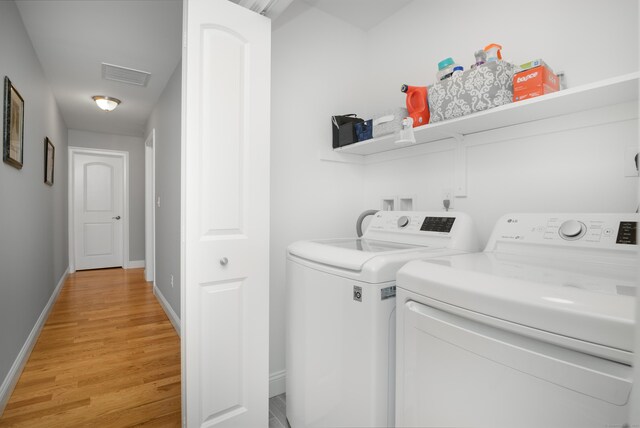 clothes washing area with separate washer and dryer and light wood-type flooring