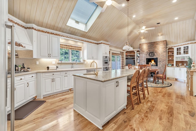 kitchen with white cabinetry, decorative light fixtures, a center island with sink, and wooden ceiling