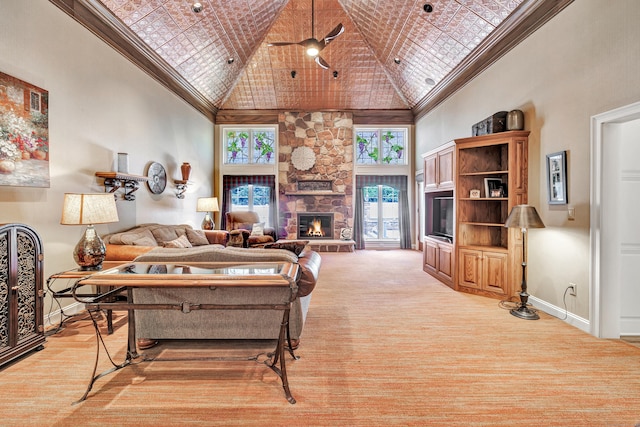 living room with a high ceiling, crown molding, a stone fireplace, and ceiling fan