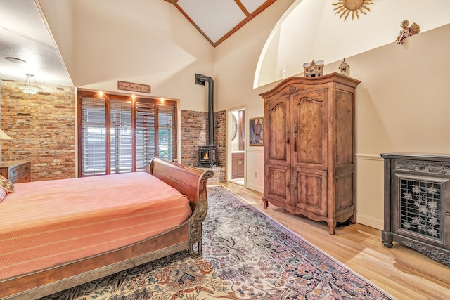 bedroom featuring crown molding, high vaulted ceiling, a wood stove, and light wood-type flooring