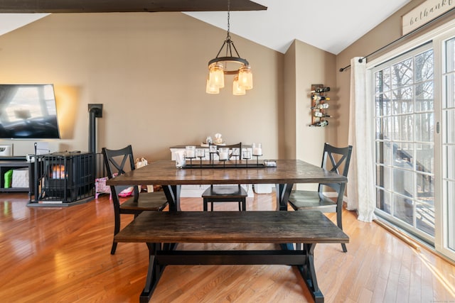 dining room featuring hardwood / wood-style flooring, vaulted ceiling, a wood stove, and a chandelier