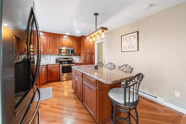 kitchen with hanging light fixtures, backsplash, stainless steel appliances, light stone countertops, and a kitchen island