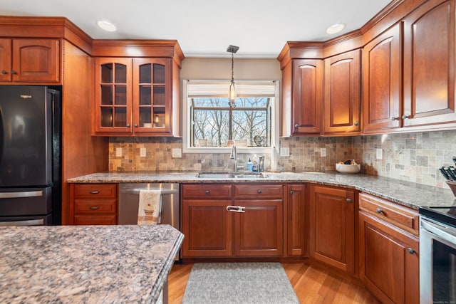 kitchen with sink, decorative backsplash, light stone counters, stainless steel appliances, and light wood-type flooring