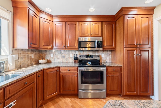 kitchen with sink, light stone counters, stainless steel appliances, light hardwood / wood-style floors, and decorative backsplash