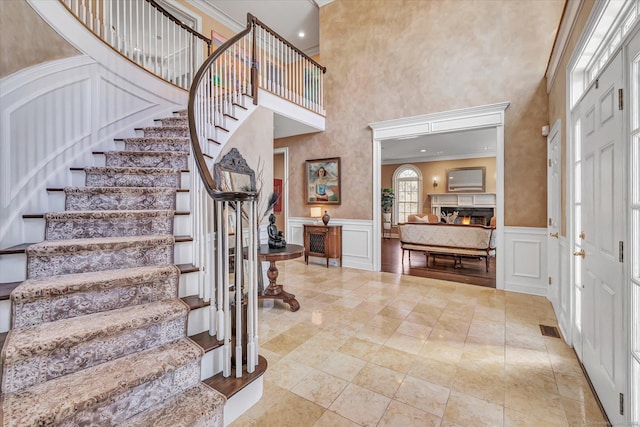 entryway with visible vents, a warm lit fireplace, crown molding, a decorative wall, and stairs