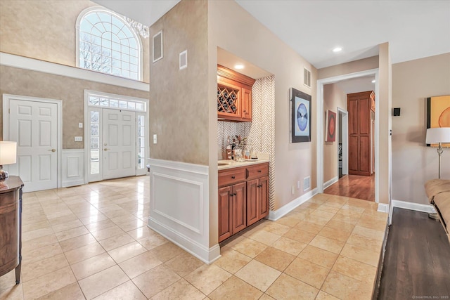 foyer with light tile patterned floors, visible vents, wainscoting, and a decorative wall