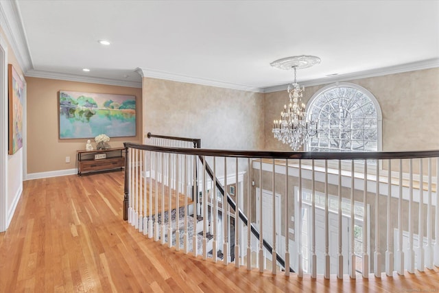 hallway with wood finished floors, baseboards, ornamental molding, a notable chandelier, and an upstairs landing