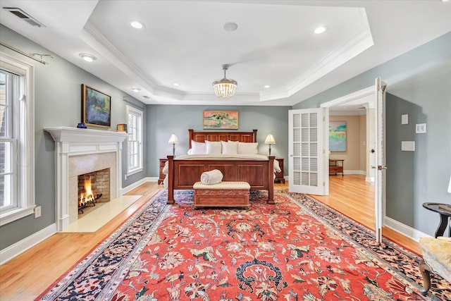 bedroom with a tray ceiling, visible vents, wood finished floors, and ornamental molding