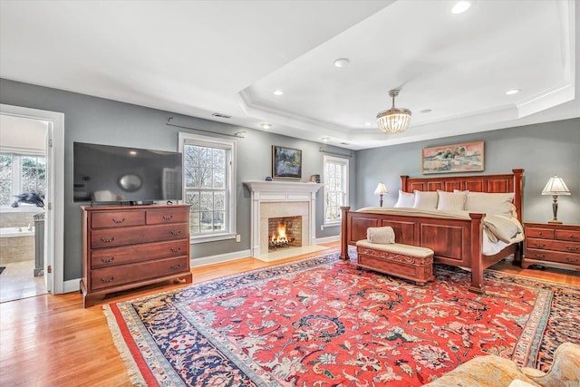 bedroom featuring visible vents, a fireplace with flush hearth, a tray ceiling, light wood finished floors, and baseboards