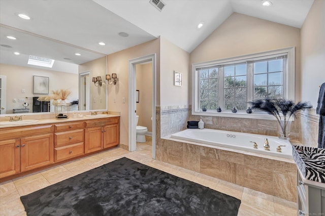 full bathroom with visible vents, toilet, a garden tub, a sink, and vaulted ceiling with skylight