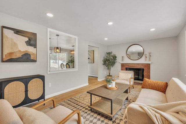 living room with a brick fireplace, a baseboard heating unit, and light hardwood / wood-style floors