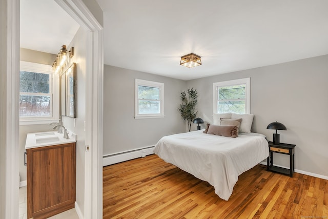 bedroom featuring multiple windows, sink, light wood-type flooring, and baseboard heating