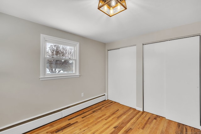 unfurnished bedroom with wood-type flooring, a baseboard heating unit, and two closets