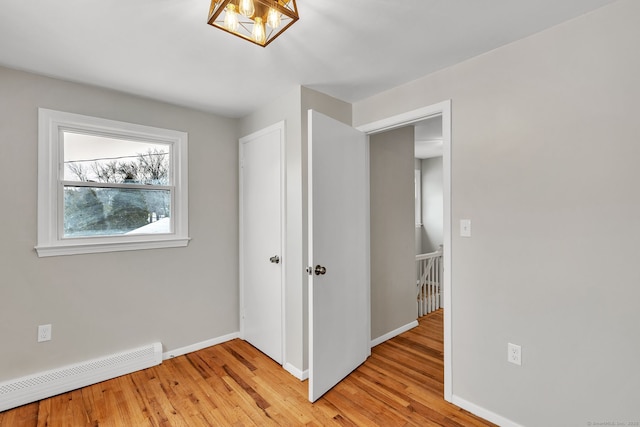 unfurnished bedroom with baseboard heating, light hardwood / wood-style floors, and a notable chandelier