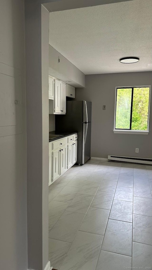 kitchen featuring a baseboard heating unit, a textured ceiling, stainless steel fridge, and white cabinets