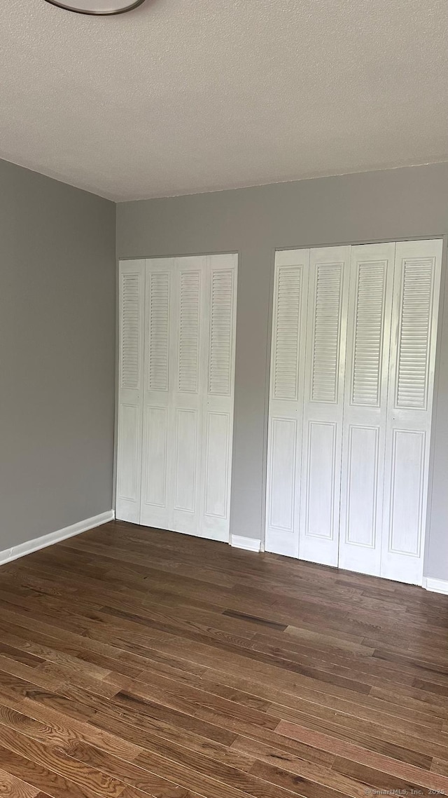 unfurnished bedroom with multiple closets, dark hardwood / wood-style flooring, and a textured ceiling