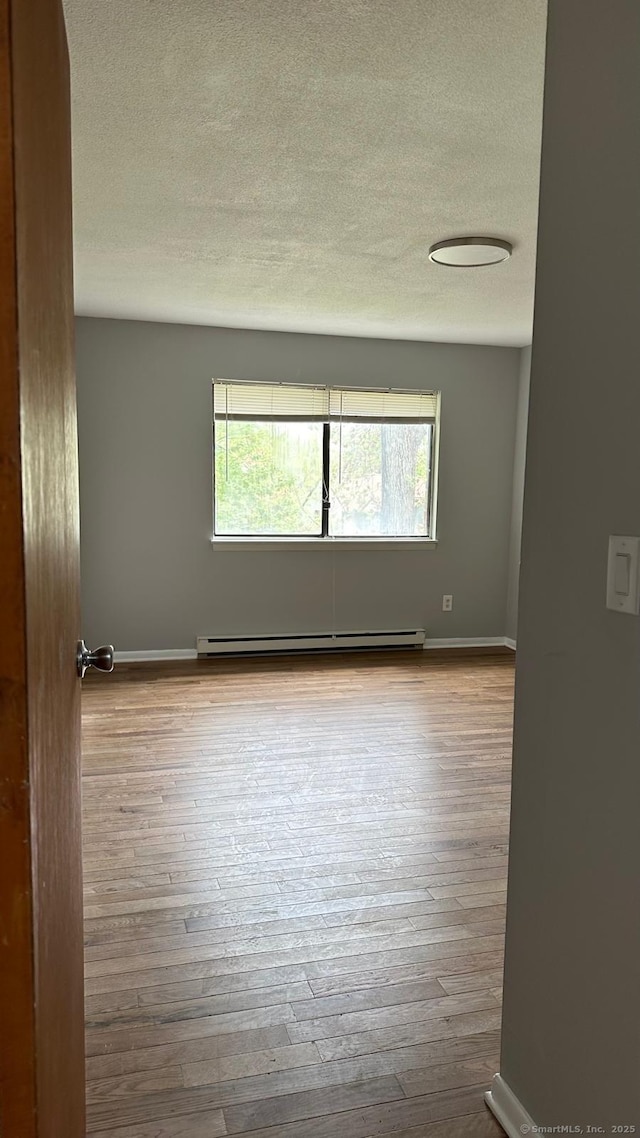 spare room with baseboard heating, light hardwood / wood-style floors, and a textured ceiling