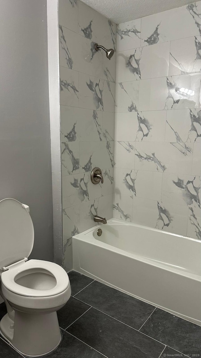 bathroom featuring a textured ceiling, toilet, and tiled shower / bath