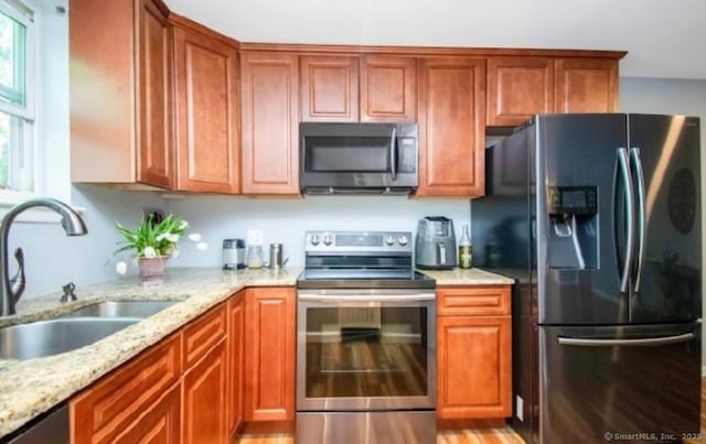 kitchen featuring appliances with stainless steel finishes, sink, light stone counters, and light hardwood / wood-style flooring