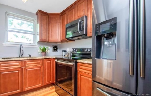 kitchen with sink, light stone countertops, light hardwood / wood-style floors, and appliances with stainless steel finishes