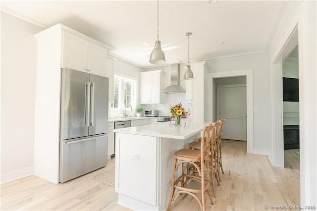 kitchen with white cabinetry, hanging light fixtures, a center island, stainless steel appliances, and wall chimney exhaust hood