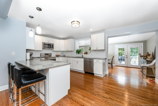 kitchen with sink, white cabinetry, decorative light fixtures, kitchen peninsula, and stainless steel appliances