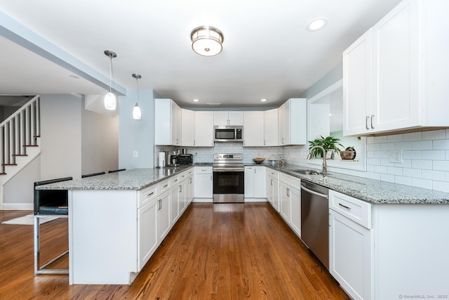 kitchen with white cabinetry, appliances with stainless steel finishes, a kitchen breakfast bar, kitchen peninsula, and pendant lighting