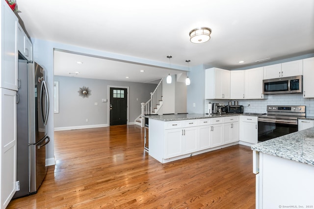 kitchen with white cabinetry, hanging light fixtures, kitchen peninsula, stainless steel appliances, and light stone countertops