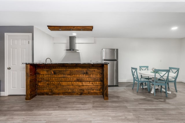 bar featuring stone counters, hardwood / wood-style flooring, stainless steel fridge, and wall chimney exhaust hood