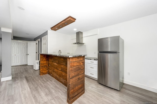 kitchen featuring wall chimney exhaust hood, white cabinetry, light hardwood / wood-style flooring, stainless steel fridge, and light stone countertops