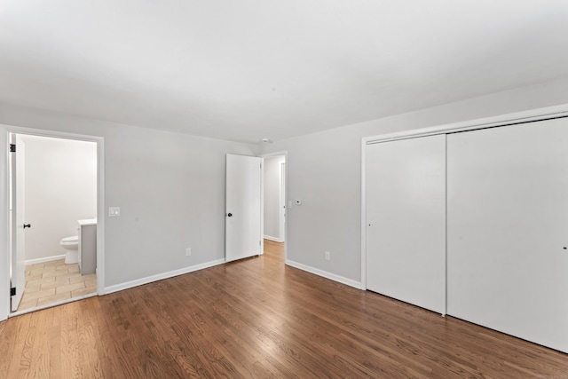 unfurnished bedroom with connected bathroom, hardwood / wood-style flooring, and a closet