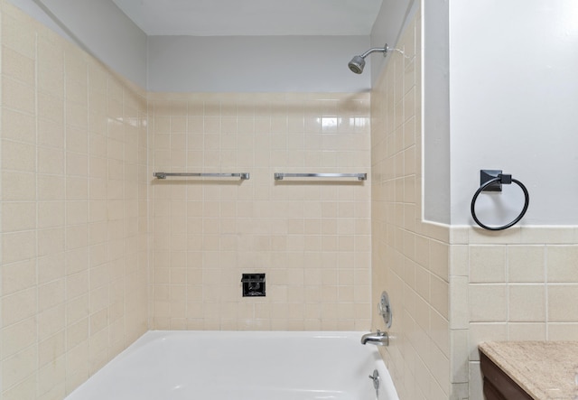 bathroom with tiled shower / bath combo, vanity, and tile walls