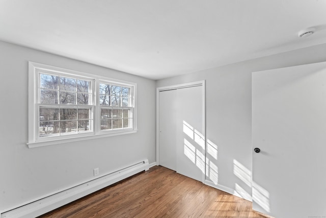 unfurnished room featuring a wealth of natural light, wood-type flooring, and baseboard heating