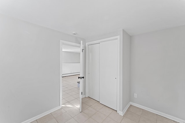 unfurnished bedroom with light tile patterned floors, baseboard heating, and a closet